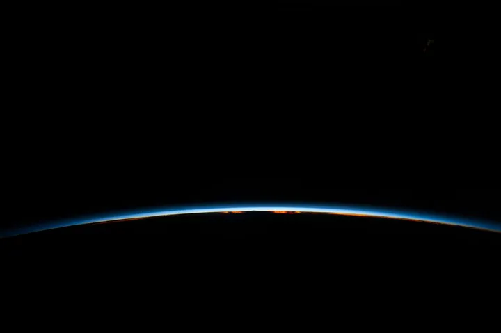 La sottile linea azzurra dell'atmosfera terrestre illuminata da un'alba orbitale, sul nero dello spazio.